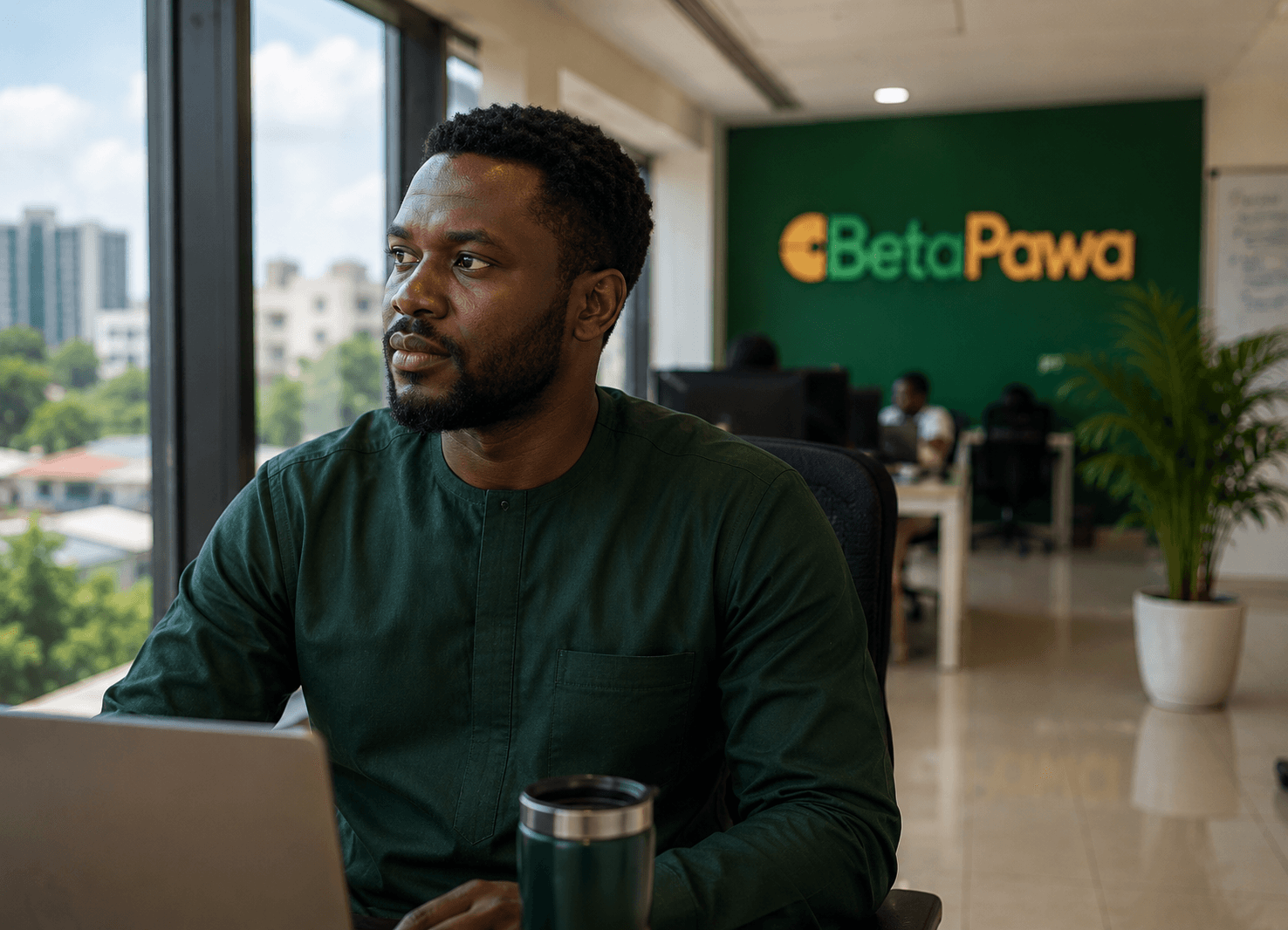A Betapawa team member at a laptop in the Lagos office, the branded green wall behind them